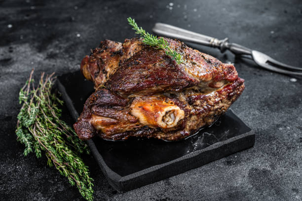 Roasted lamb bone-in leg on a cutting tray, garnished with fresh herbs