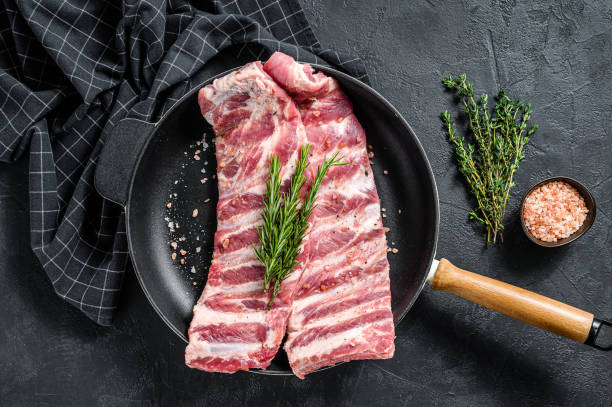 Raw lamb spare ribs with visible bone and fat marbling, topped with herb sprig.