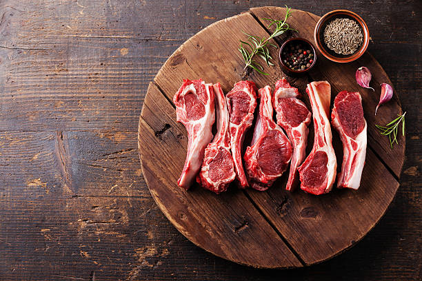 Raw lamb rib chops on wooden board with rosemary and spices