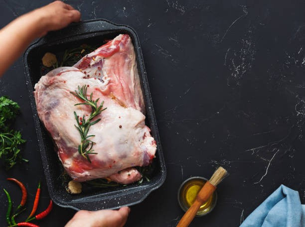 Raw lamb shoulder roast with rosemary sprig in black tray