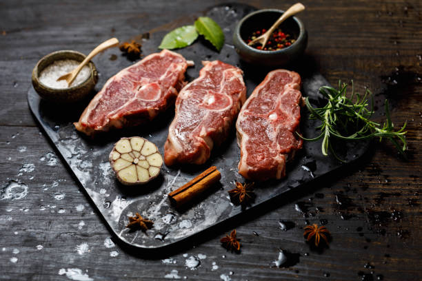 Raw lamb loin chops on a slate board with rosemary and garlic clove