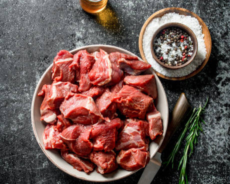Bowl of raw lamb stew meat, red chunks with visible marbling and bone pieces
