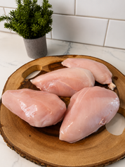Raw boneless skinless chicken breasts on wooden cutting board