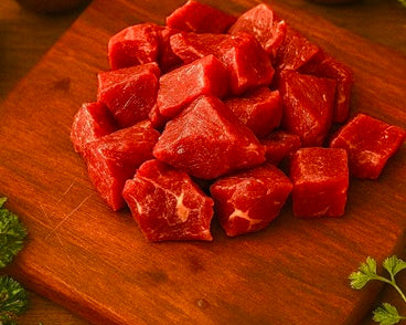 Beef stew meat, raw red cubed chunks on wooden cutting board