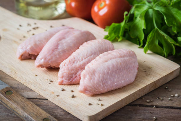 Raw chicken wing pieces on a wooden cutting board with herbs and pepper
