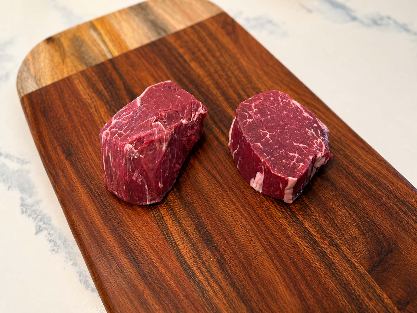 Filet mignon steaks, two raw beef medallions on a wooden cutting board.