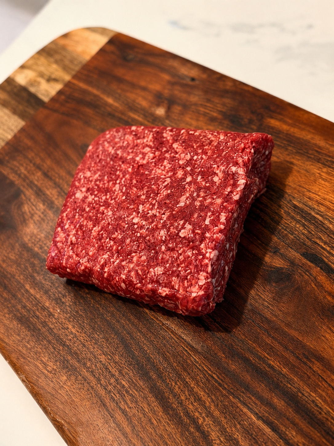 Raw ground beef loaf, marbled red and white texture on wooden board.