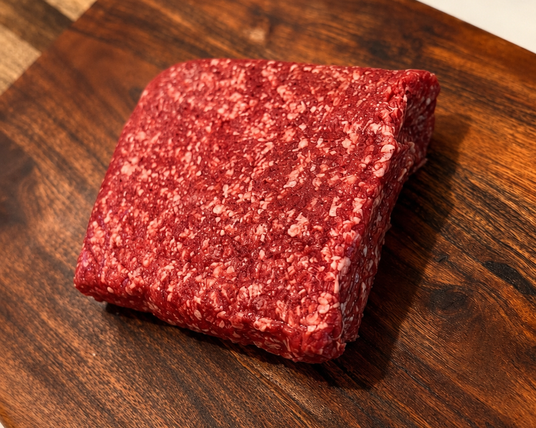 Raw ground beef loaf, marbled red and white texture on wooden board.