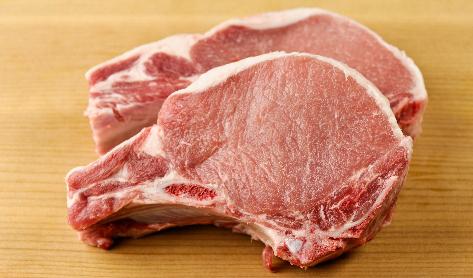 Raw bone-in pork chops, pink-red meat with marbling