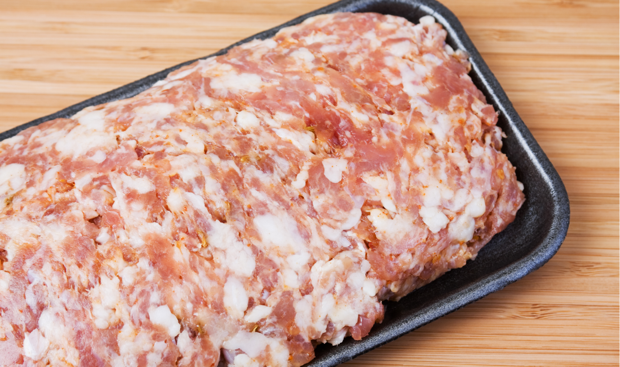 Raw pork sausage on black tray, sliced pieces with visible white fat