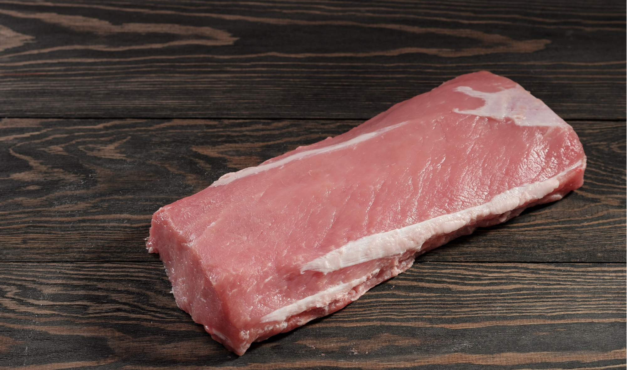 Raw pork tenderloin piece with visible fat cap on a dark surface
